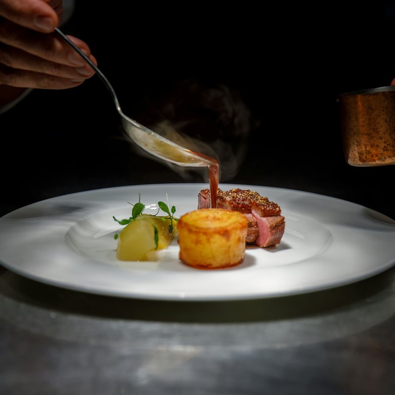 Le chef nappe de sauce une assiette au passe, sur fond sombre